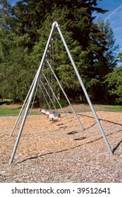 A Large Toddler Swing Set In A Beautiful Park Over Bark Mulch For Safety.