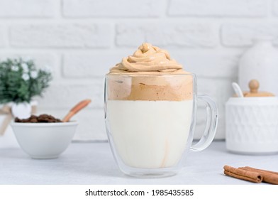Large transparent mug with Dalgona coffee. Nicely and neatly laid out whipped coffee foam in cold milk. Dalgona, coffee beans, milk bottle, sugar bowl and cinnamon sticks on a light background.