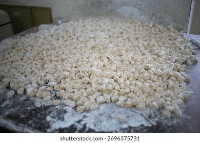 A large tray filled with tiny, flour-dusted dough balls ready for baking in a commercial bakery. Fresh, artisanal treats prepared for cookies or pastries in a busy production setting.