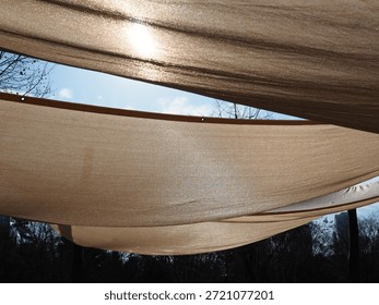 Large triangular sunshades filter bright sunlight in a park under a clear blue sky with tall trees.