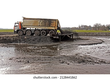 Large truck with tipper trailer unloads its freight of dredging spoil, sludge, sediment into a storage compartment  or depot)