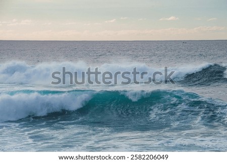 Large turquoise waves roll in the foreground, a small boat is visible on the horizon, and pastel toned clouds fill the sky in a coastal Hawaii scene.