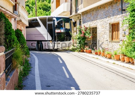 A large type bus is making a tight turn on a very narrow street in a village on Crete