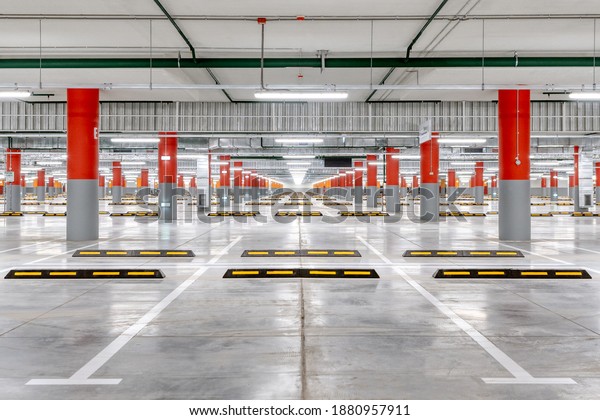 Large\
underground parking for cars. Empty new parking lot with bright\
lighting. The columns are painted red and\
orange.