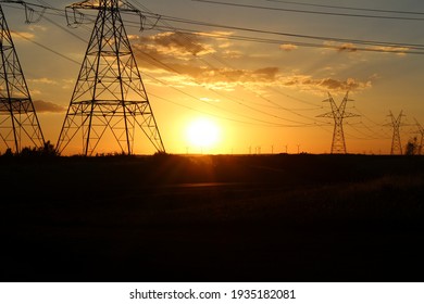 Large utility power line towers in the foreground and wind turbines in the background at sunset in West Texas