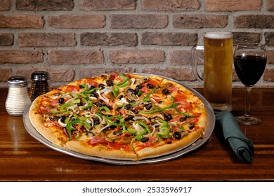 A large vegetable pizza with a glass of beer and a glass of red wine on a wooden table against a brick wall. - Powered by Shutterstock