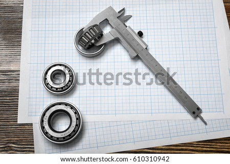 A large vernier scale lying on cross section paper with three bearings around it on wooden background. Engineering and repair. Workshop environment. Building tools and equipment.