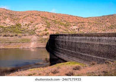 A large wall of stone sits next to a body of water. The water is calm and still, reflecting the surrounding landscape. Concept of tranquility and serenity, as the wall and water create a peaceful