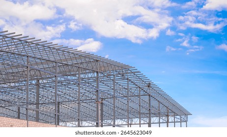 Large warehouse industrial factory building framework with welders are welding metal roof beam structure in construction site against blue sky background, low angle and perspective side view