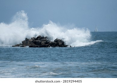 A large wave crashes and splashes dramatically over a rock jetty near Venice Beach, California.
