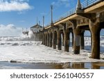 Large waves crash into the Manhattan Beach pier in Los Angeles, California during high surf advisory and pier closure.