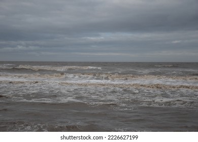 Large waves crashing onto the beach and sea wall during high tide with a cloudy sky background. Taken in Cleveleys Lancashire England. 