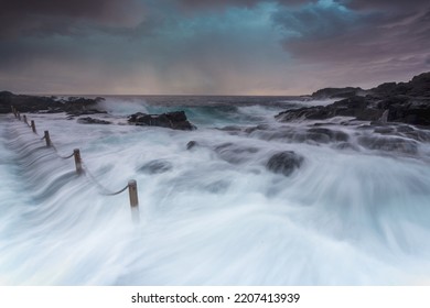 Large Waves Volume Of Water Flowing Over Rocks Into Rock Pool, Long Exposure Showing The Water Flow.  Overhead Storm Clouds And A  Sunrise.