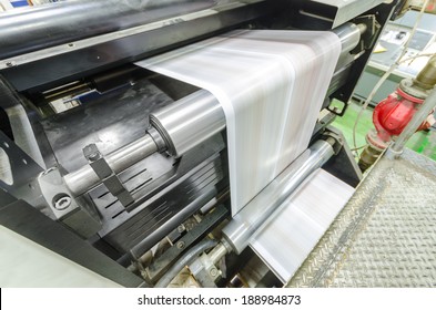 A large webset offset printing press running a long roll off paper over its rollers at high speed. - Shutterstock ID 188984873