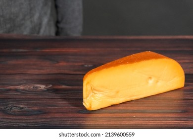 Large Wedge Of Smoked Gouda Cheese On A Dark Wooden Background.