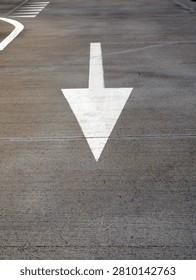 A large white arrow points down on a concrete surface. There are other white painted lines on the surface, including a curved line and a crosswalk pattern.