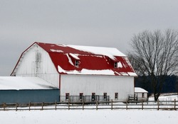 A Large White Barn With A Red Roof, And A Side Farm Building Of Blue, Both Behind Wood Fences On A Snowy Winter Day In The Country