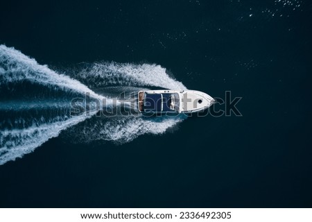 A large white boat with a blue awning is moving fast on dark water. Top view. Big white motor yacht movement on dark water top view.