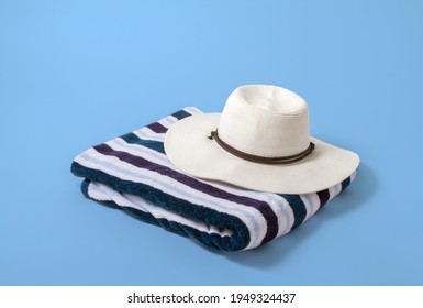 Large White Brim Hat On A Striped Beach Towel With A Light Blue Background