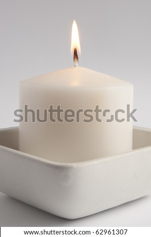 Large white candle in a square tray close up