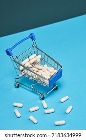 Large White Capsules Crumbled From The Supermarket Trolley, The Rest Are In The Supermarket Trolley. White Pills Are Lying On A Blue Background