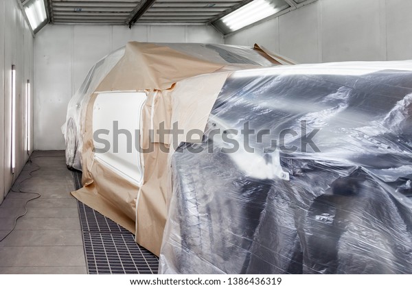 A large white car is completely covered in paper\
and adhesive tape to protect against splash during painting and\
repair after an accident in a workshop for body repair of vehicles\
with bright lighting