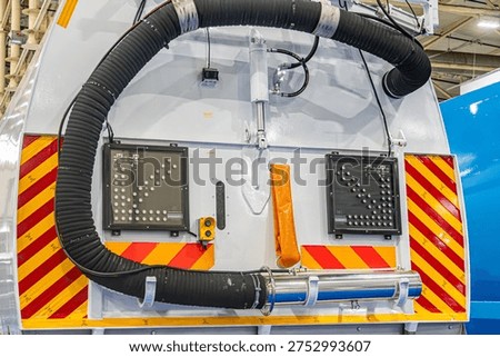 A large white circular mechanical component with ventilation holes, accompanied by two rectangular red-striped panels with controls, and an upward-extending black hose The setting is unspecified wit