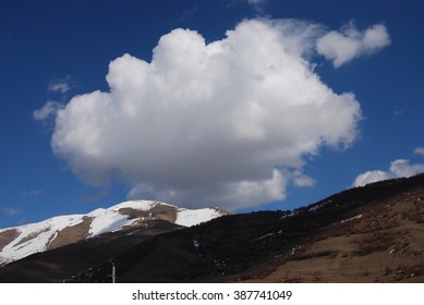 A large white cumulus cloud floating over a snow-covered mountain peak against a clear blue sky