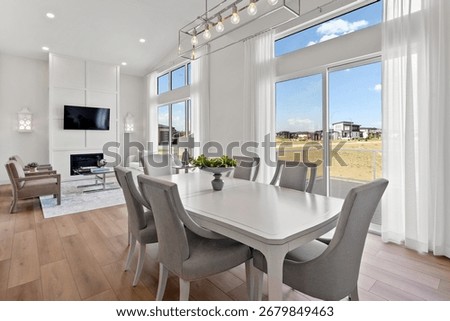 Large white dining table with a white tablecloth and gray chairs is set in a living room. The room has a modern and elegant design, with a fireplace and a large window that lets in natural light