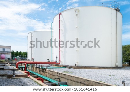 Large white industrial tanks for petrochemical or oil or fuel or water in refinery or power plant or industrail plant and red fire fighting pipelines on the side of the tank on blue sky background.