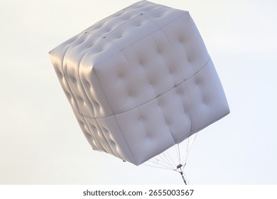 large white inflatable cube floating against a pale overcast sky backdrop