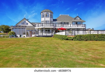 Large White Inn Craftsman Style Home With Blue Sky And Green Grass.