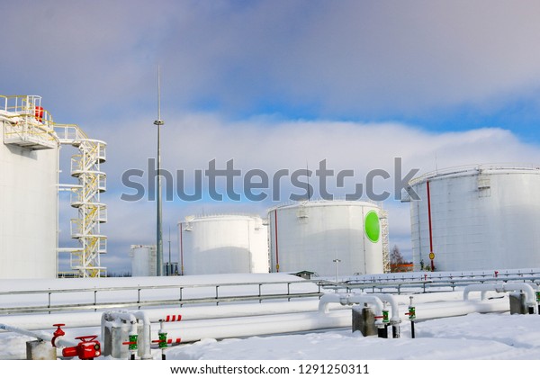 Large white iron metal industrial tanks for\
storage of fuel, gasoline and diesel and pipeline with valves and\
flanges at the refinery in the\
winter.