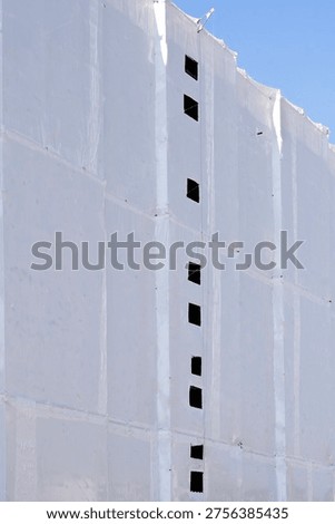 Large white protective plastic sheets cover the entire facade of a building under renovation with a vertical row of small square openings