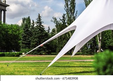 A large white tent is stretched on a lawn in the center of the city