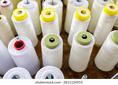 Large white thread spools sit mounted on metal rods in a textile workshop, this thread arrangement shows colorful tops in neat rows, the thread spools create an industrial pattern ready for production