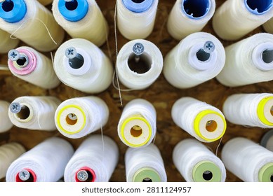 Large white thread spools sit mounted on metal rods in a textile workshop, this thread arrangement shows colorful tops in neat rows, the thread spools create an industrial pattern ready for production