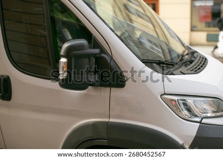 A large white van is parked securely on the side of the road right in front of a tall building, creating a distinct presence in the area
