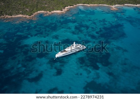 Large white yacht along the coastline at anchor. Large white modern mega yacht on transparent blue water, anchorage top view.