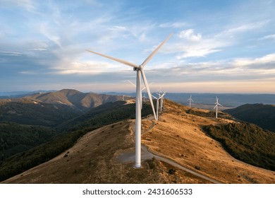 Large wind turbines with blades in field aerial view bright orange sunset blue sky wind park slow motion drone turn. Silhouettes windmills, large orange sun disc summer lens flare. Alternative energy - Powered by Shutterstock