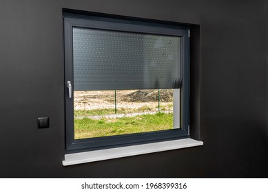 A large window in a room with black walls, half covered with external blinds.
