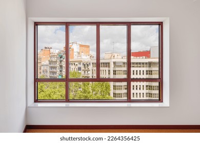 Large window in the room with a wide window sill. Window in plastic brown frame. Through the window you can watch what is happening on the street and the neighboring houses opposite.