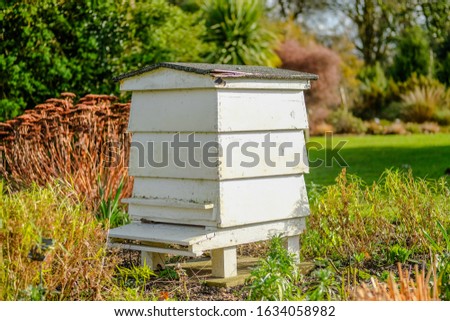 Large wooden Beehive seen located in a large garden. The well maintained lawn and shrubs are clearly evident.