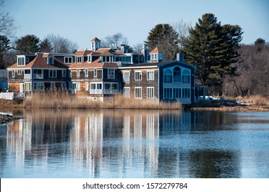 A Large Wooden Building Reflecting On The Kennebunk River In Kennebunkport Maine On A Clear Blue Sky Winter Day. 