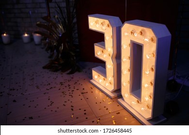 Large wooden figures for the anniversary of 30 years with luminous bulbs inside stand on the floor in a restaurant. Decor for the celebration of the anniversary of the man. Adult guy's birthday