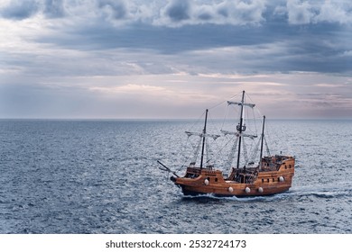 A large wooden sailing ship cruising across a calm sea. The vessel has tall masts with sails furled, suggesting it's either traveling leisurely or preparing for a journey. The sky is overcast.  - Powered by Shutterstock