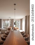 Large wooden table in a dining room. Around it beige-brown armchairs very comfortable. In the background is the living room.