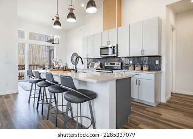 large working chefs kitchen with long white granite counter top hardwood floors grey cabinets stainless appliances large view windows dining table set for dinner