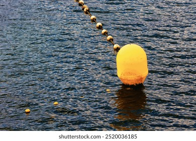 A large yellow buoy floats on the water, accompanied by a line of small floats that form a barrier on the water surface.  - Powered by Shutterstock