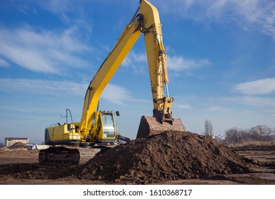a large yellow crawler excavator with an arrow and a bucket in the foreground near a pile of earth beautifully backlit by the sun at a construction site in against a blue sky